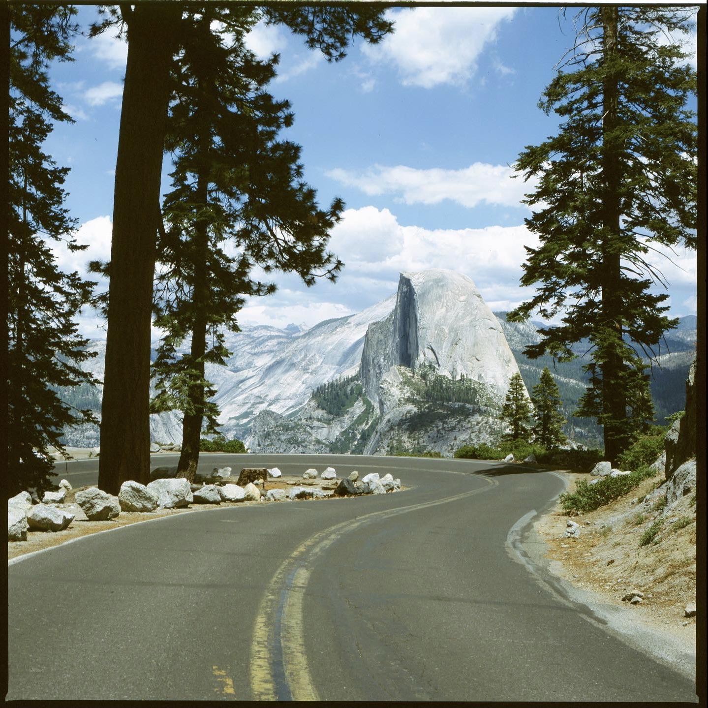 A winding road leads through a forest towards a large mountain.