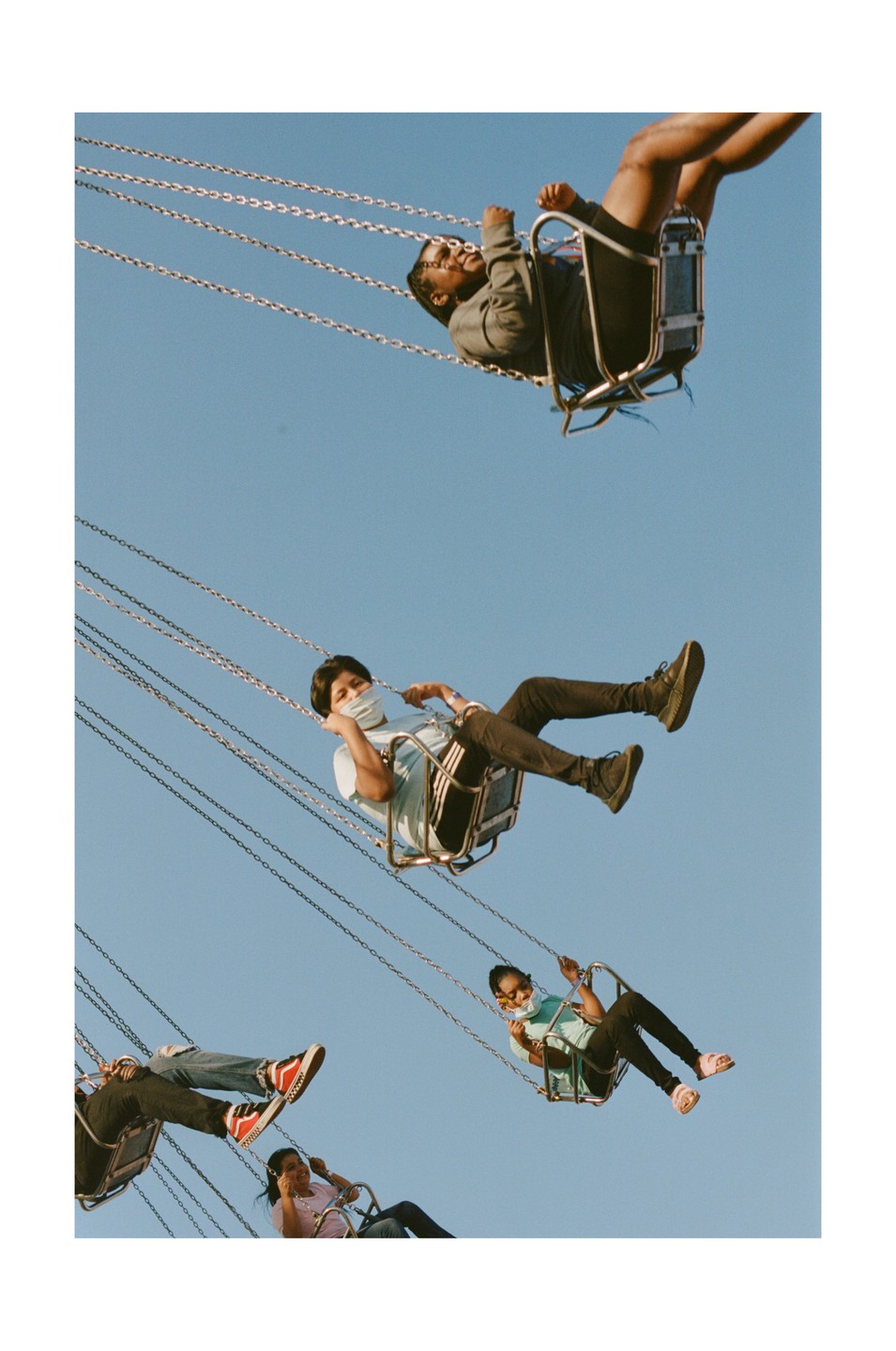 Four people are riding a swing ride against a clear blue sky.