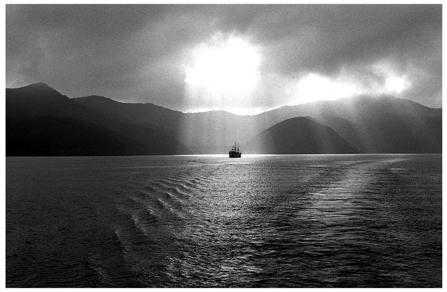 A boat sails on a lake with mountains in the background under a bright sky.