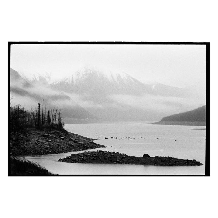 A body of water is surrounded by rocky shores and mountains covered in snow and fog.