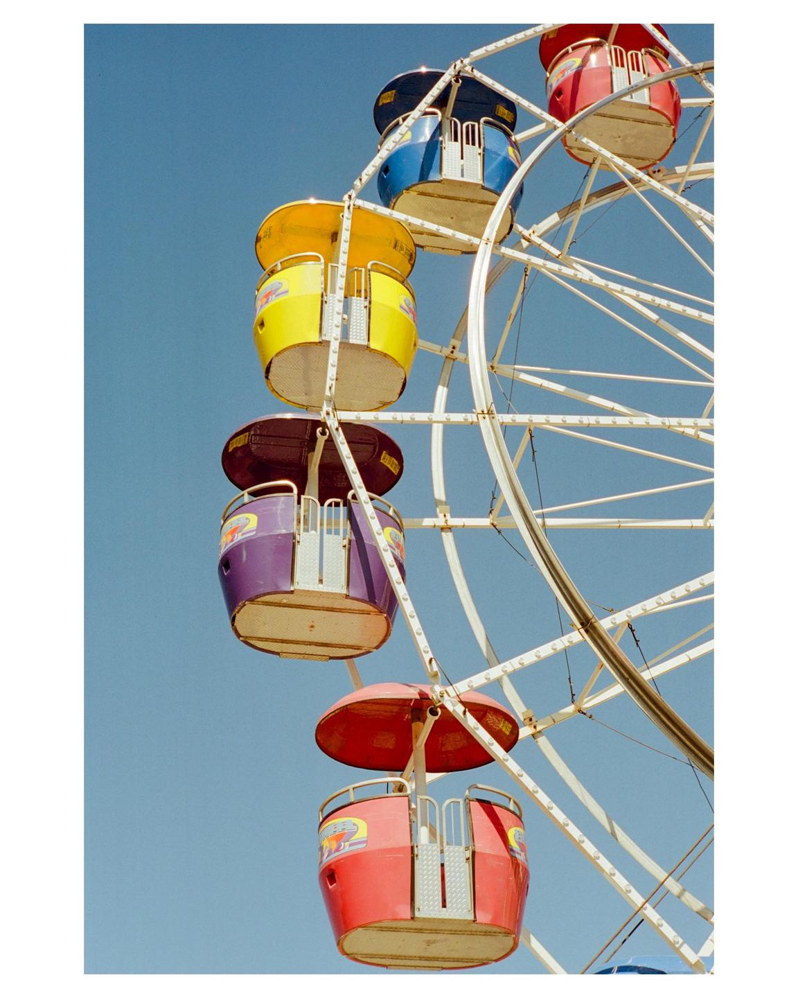 A colorful ferris wheel with multiple gondolas is set against a clear blue sky.
