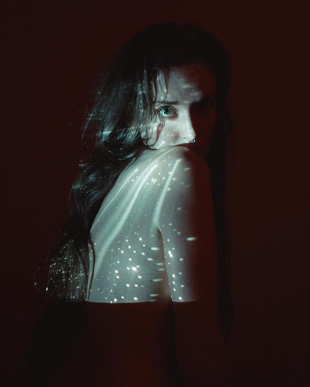 A woman with long hair looks over her shoulder, with light projected onto her back.