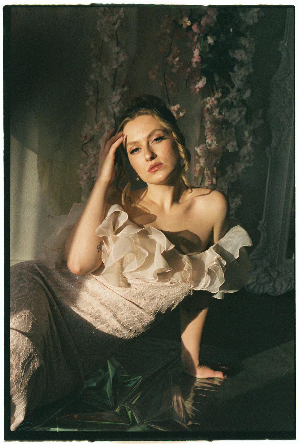 A woman in a ruffled dress sits on the floor with light falling on her face and body.