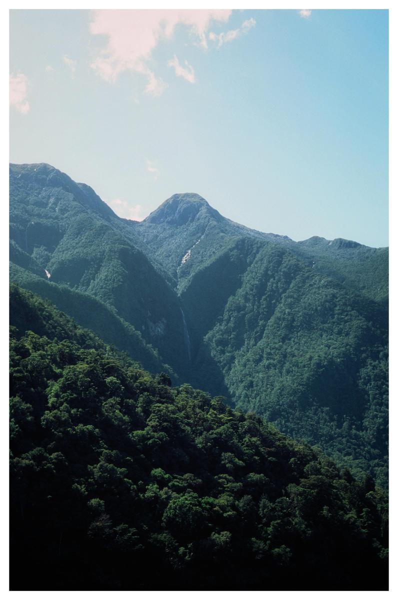 A lush green mountain range is visible under a clear blue sky with a few clouds.