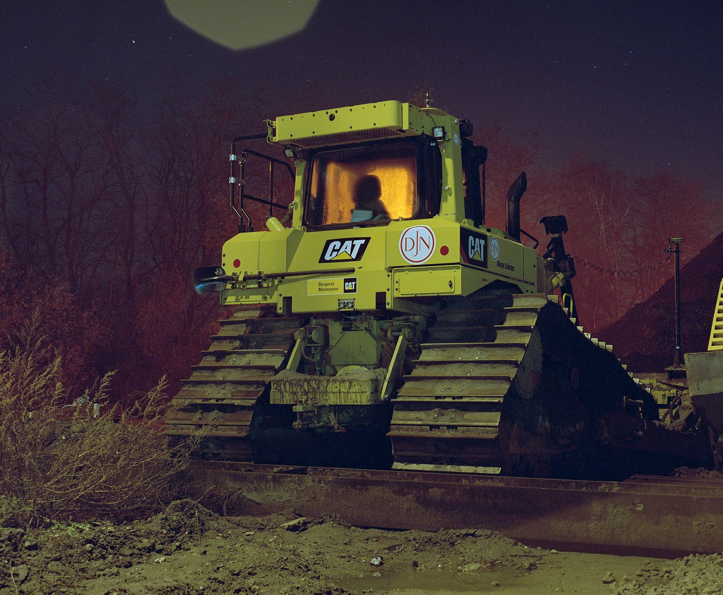 A yellow bulldozer is parked on a dirt construction site at night.