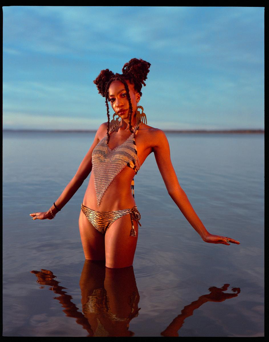 A woman in a bikini stands in water with her arms outstretched.