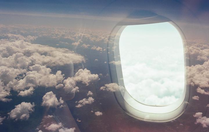 A double exposure shows a view of clouds from an airplane window and a landscape with clouds.