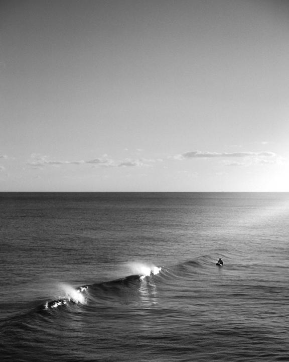 A surfer sits on a surfboard in the ocean as a small wave breaks nearby.