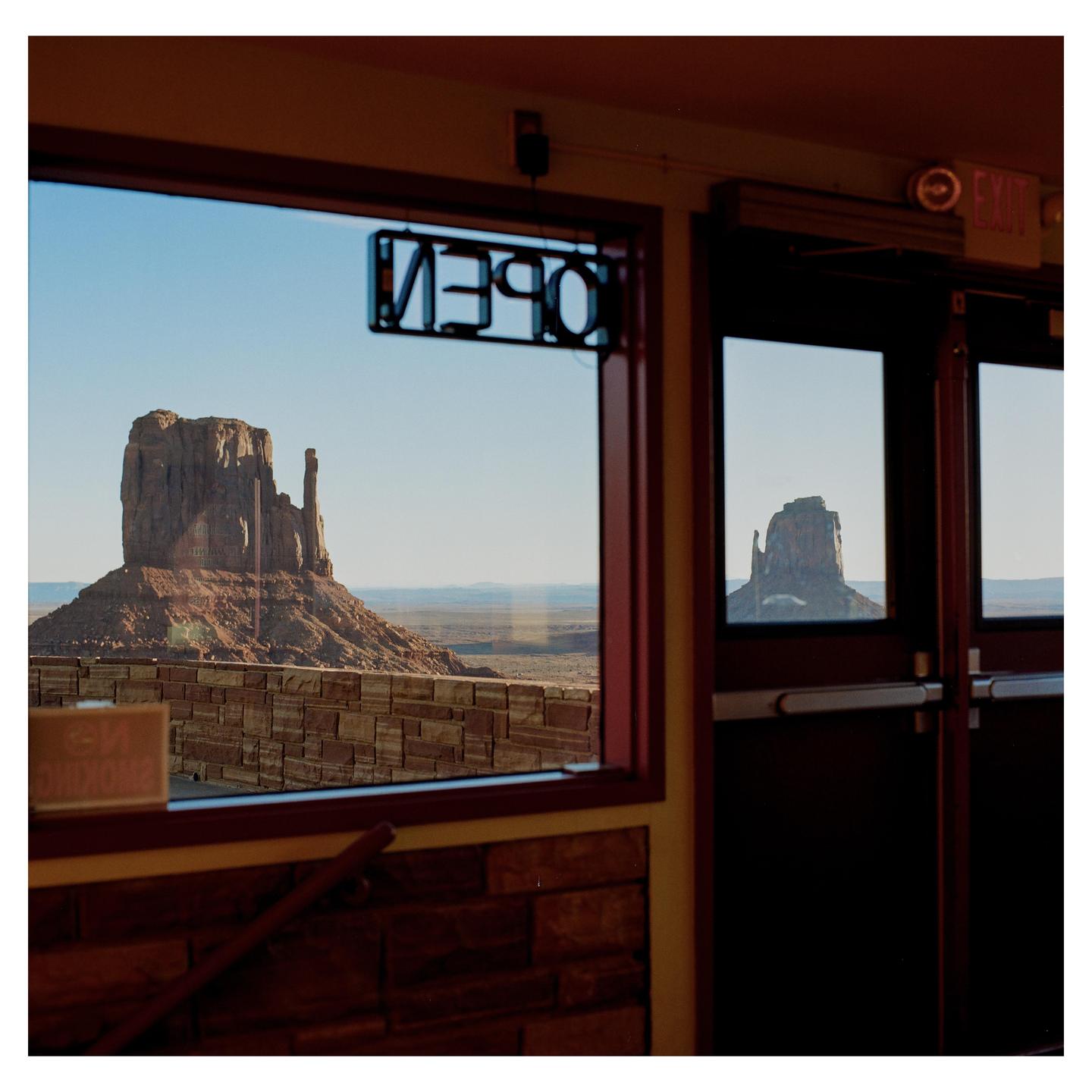 A rock formation in a desert landscape is visible through a window with an "OPEN" sign.