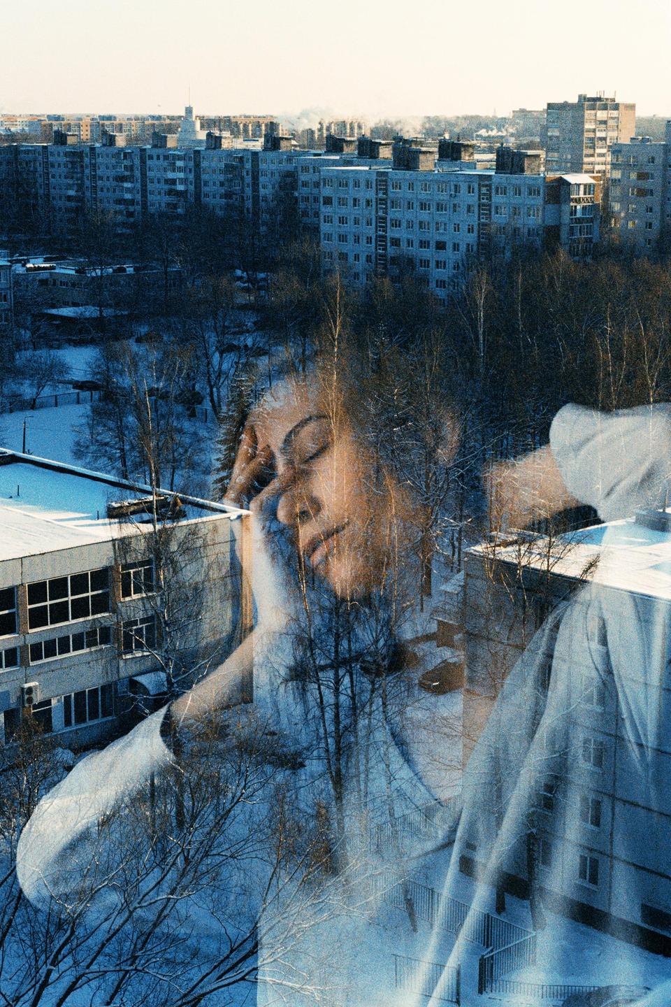 A woman's face is double exposed over a snowy urban landscape with apartment buildings and trees.