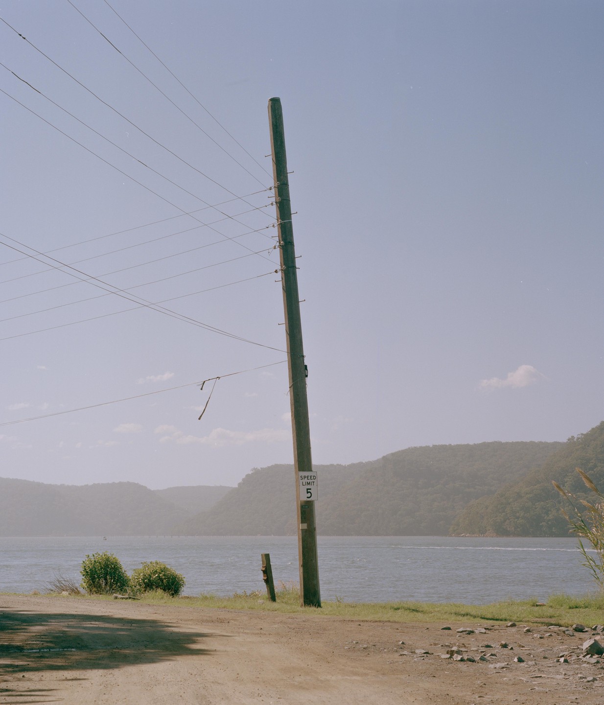 A utility pole with a speed limit sign stands beside a body of water with hills in the background.