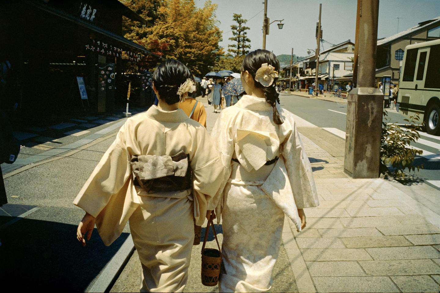 Two women in kimonos walk away from the viewer on a street in Kyoto.