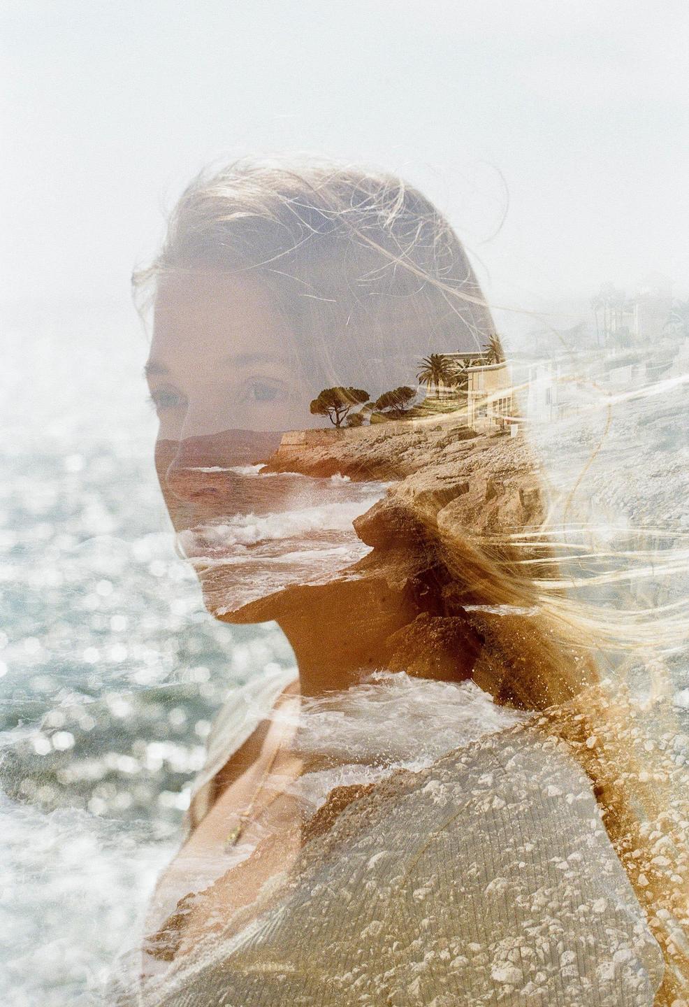 A woman's profile is double exposed with a rocky coastline and ocean waves.