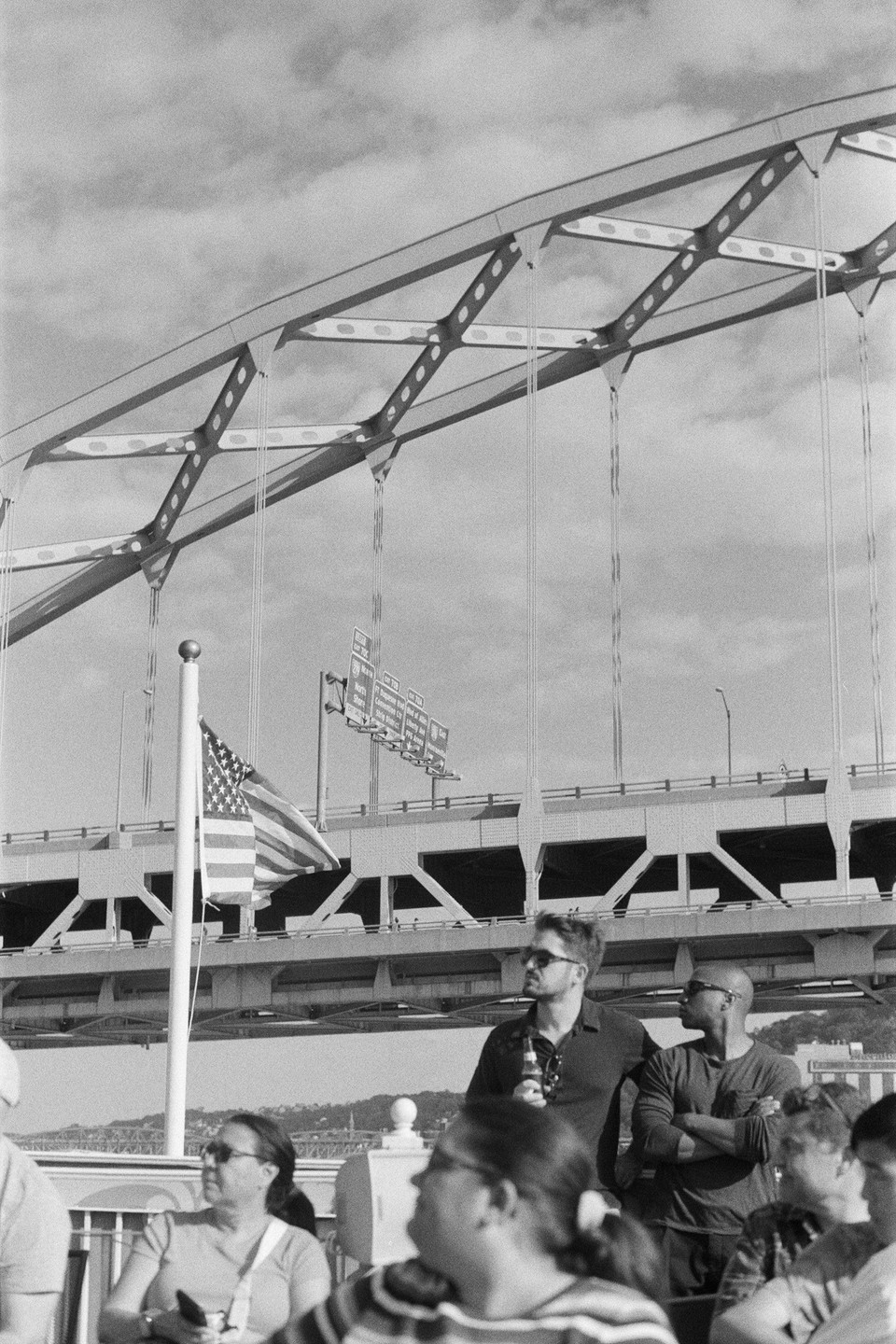 A group of people are on a boat with a bridge and an American flag in the background.