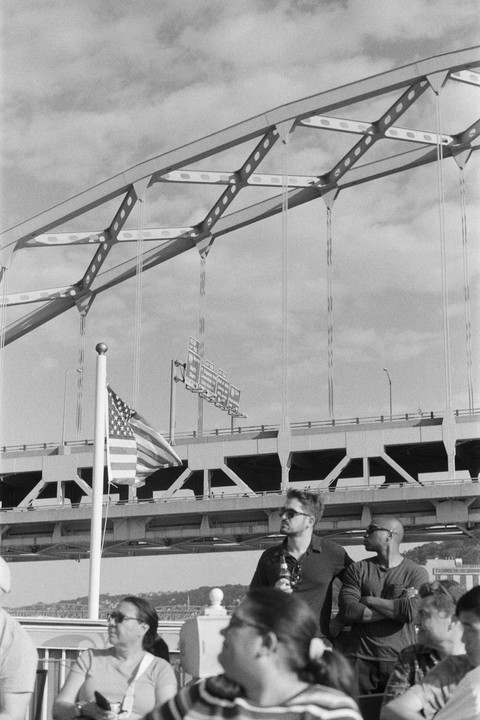 A group of people are on a boat with a bridge and an American flag in the background.