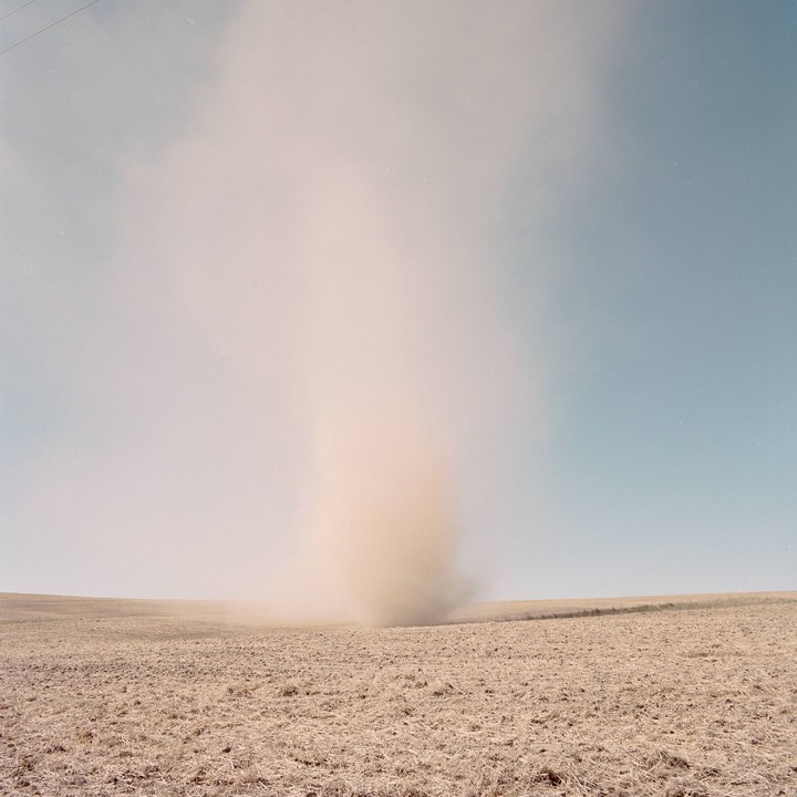A dust devil swirls in a field under a hazy sky.