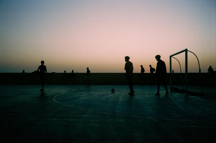Silhouetted men play soccer on a court at dusk.