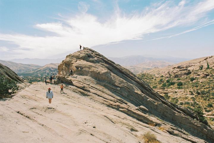 A group of people are climbing a large rock formation in a desert landscape.
