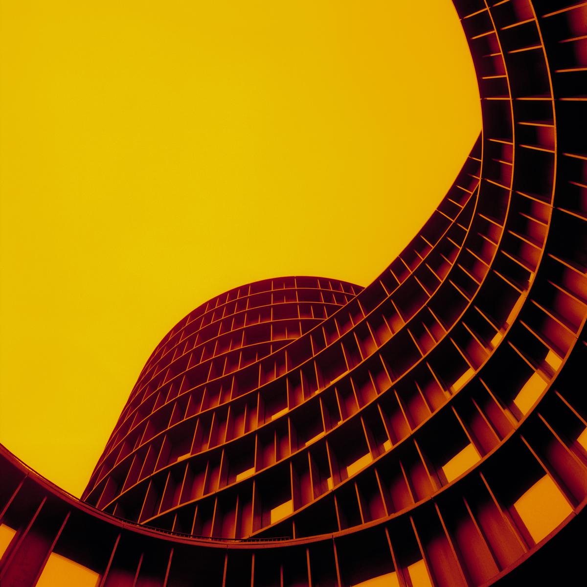 A low-angle view shows the curved facade of a building against a bright yellow sky.