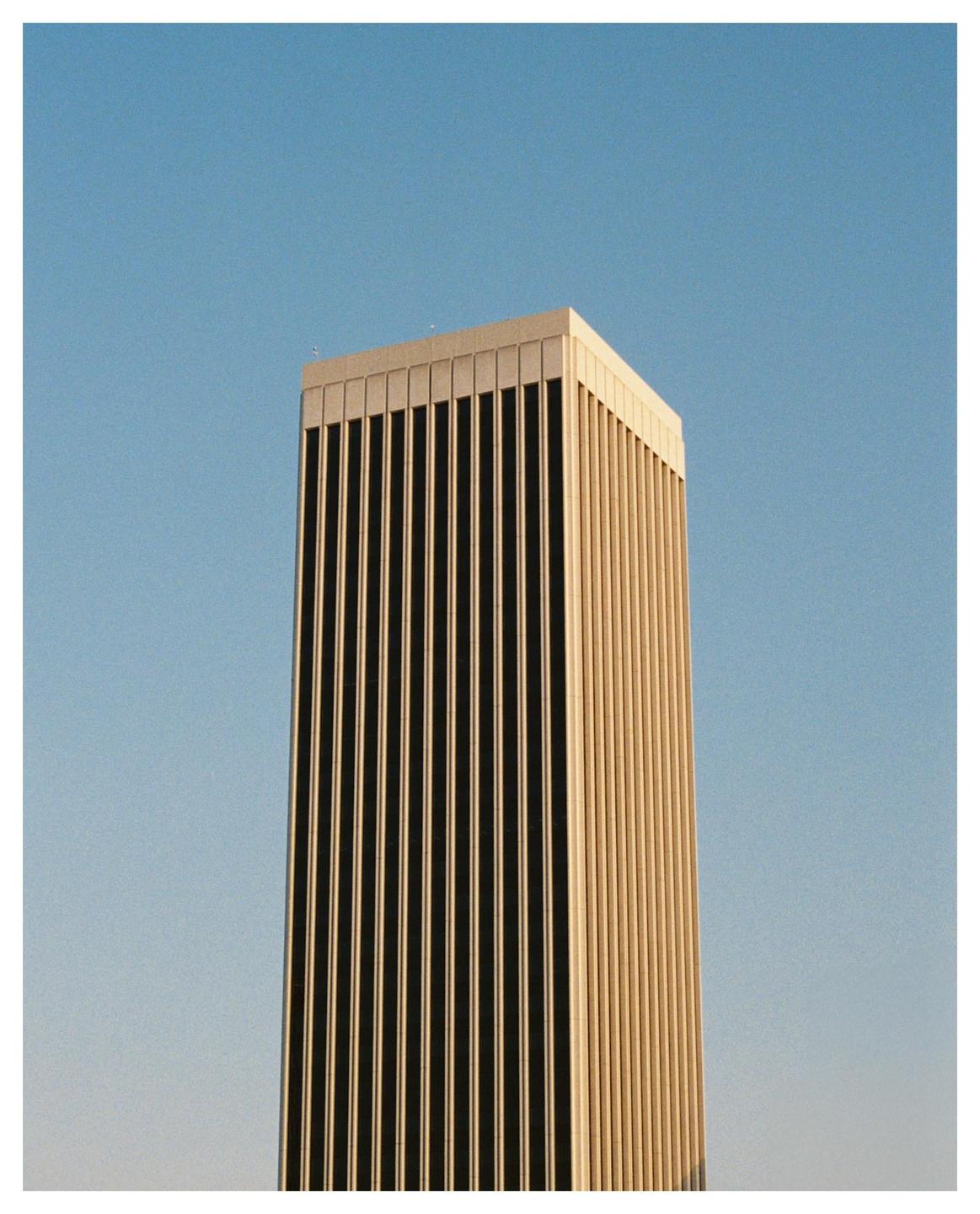 A tall, modern building with vertical lines on its facade stands against a clear blue sky.