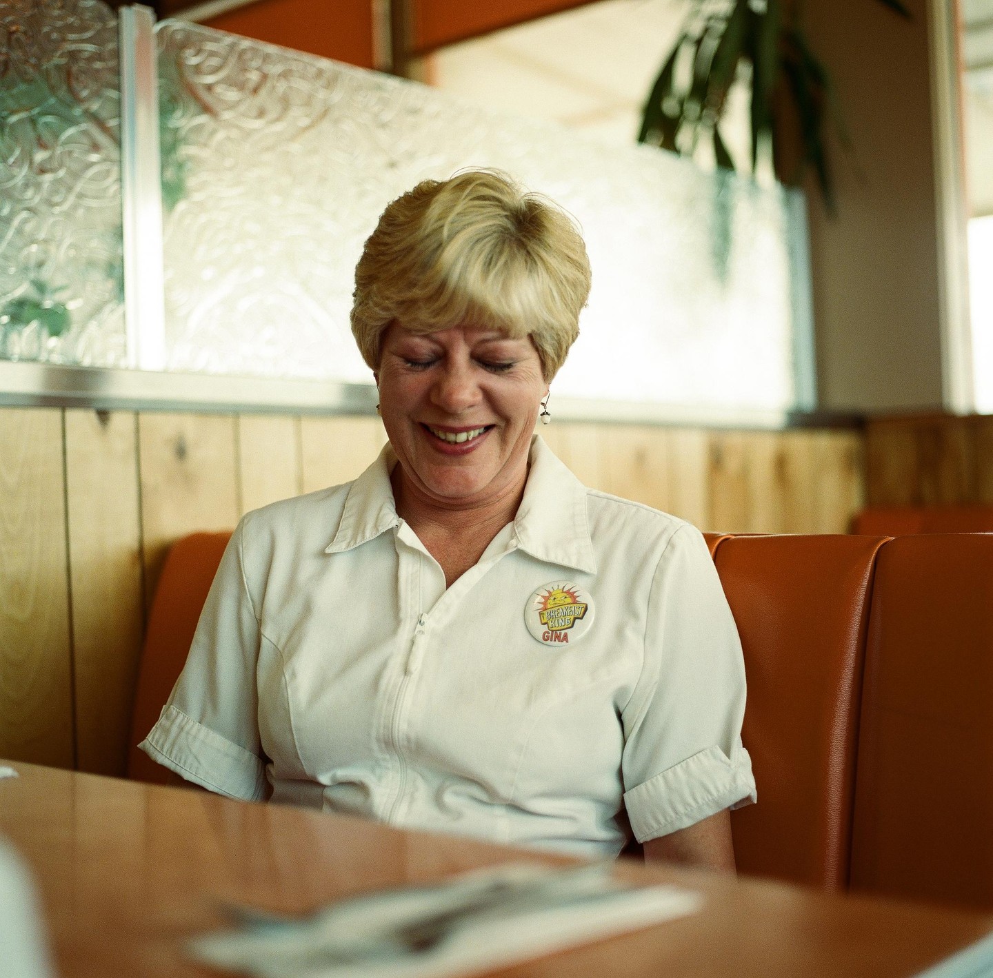 A woman with short blonde hair smiles while sitting in a diner booth.