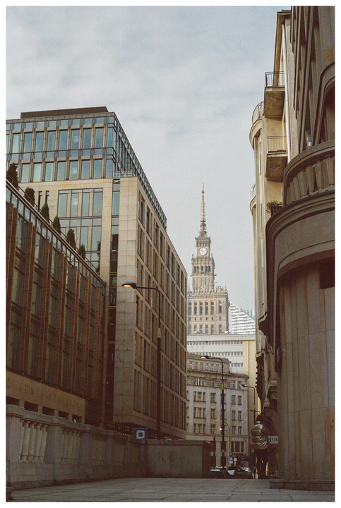 A tall, ornate clock tower rises above other buildings on a city street.