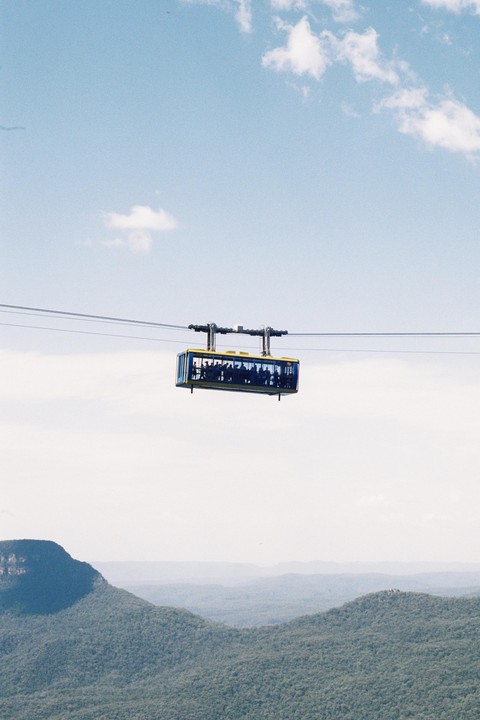 A cable car full of people travels across a valley with mountains in the background.