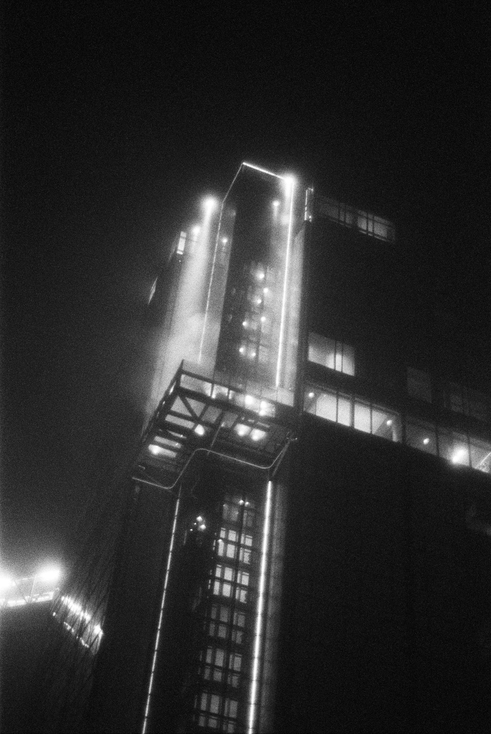 A tall building with bright lights is visible through a hazy night.