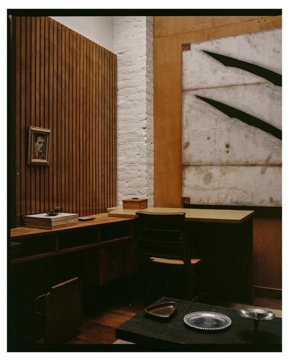 A room with wooden walls, a desk, a chair, and a painting of a man on the wall.