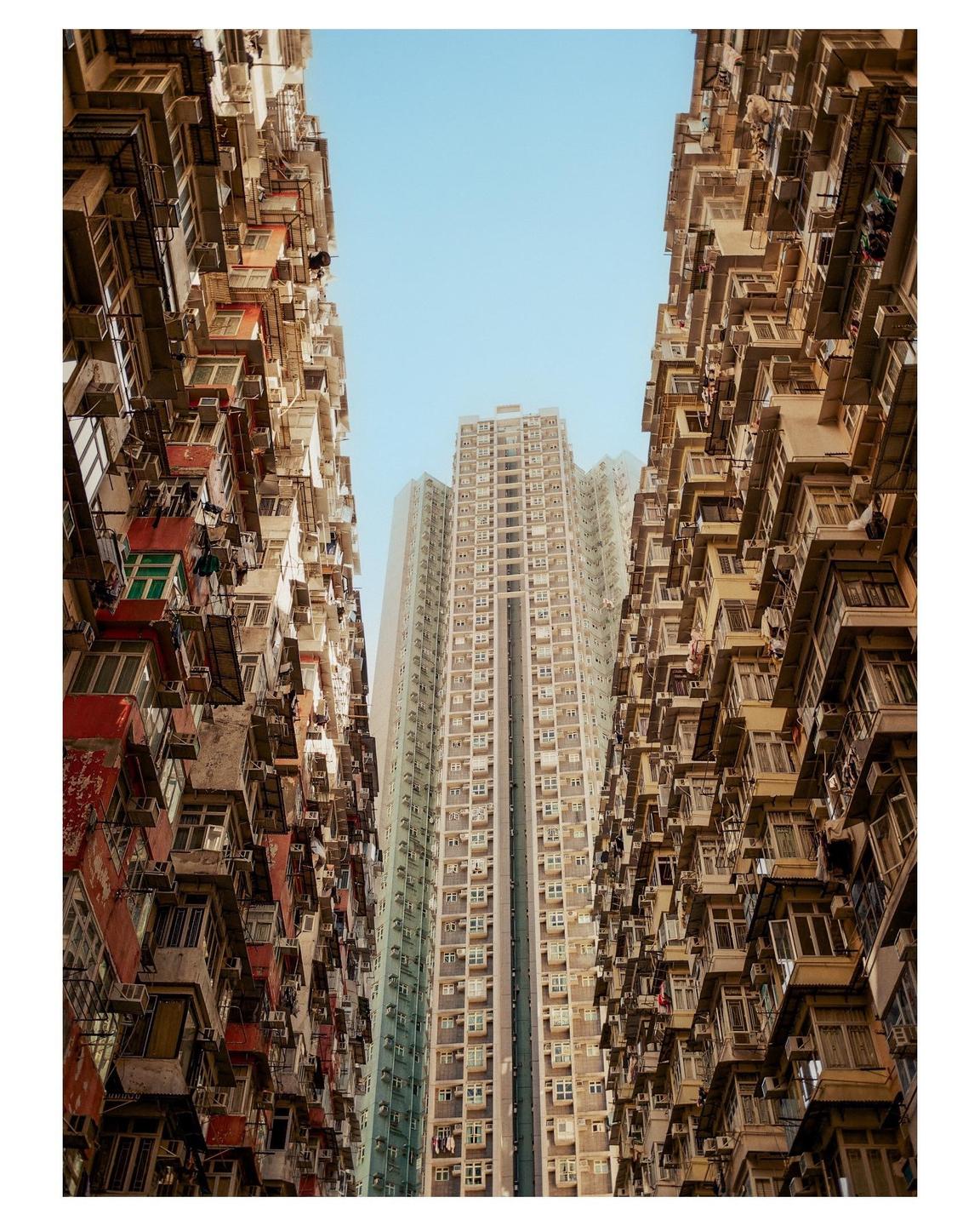 A low-angle view shows a tall, modern building framed by two older, densely packed residential buildings.