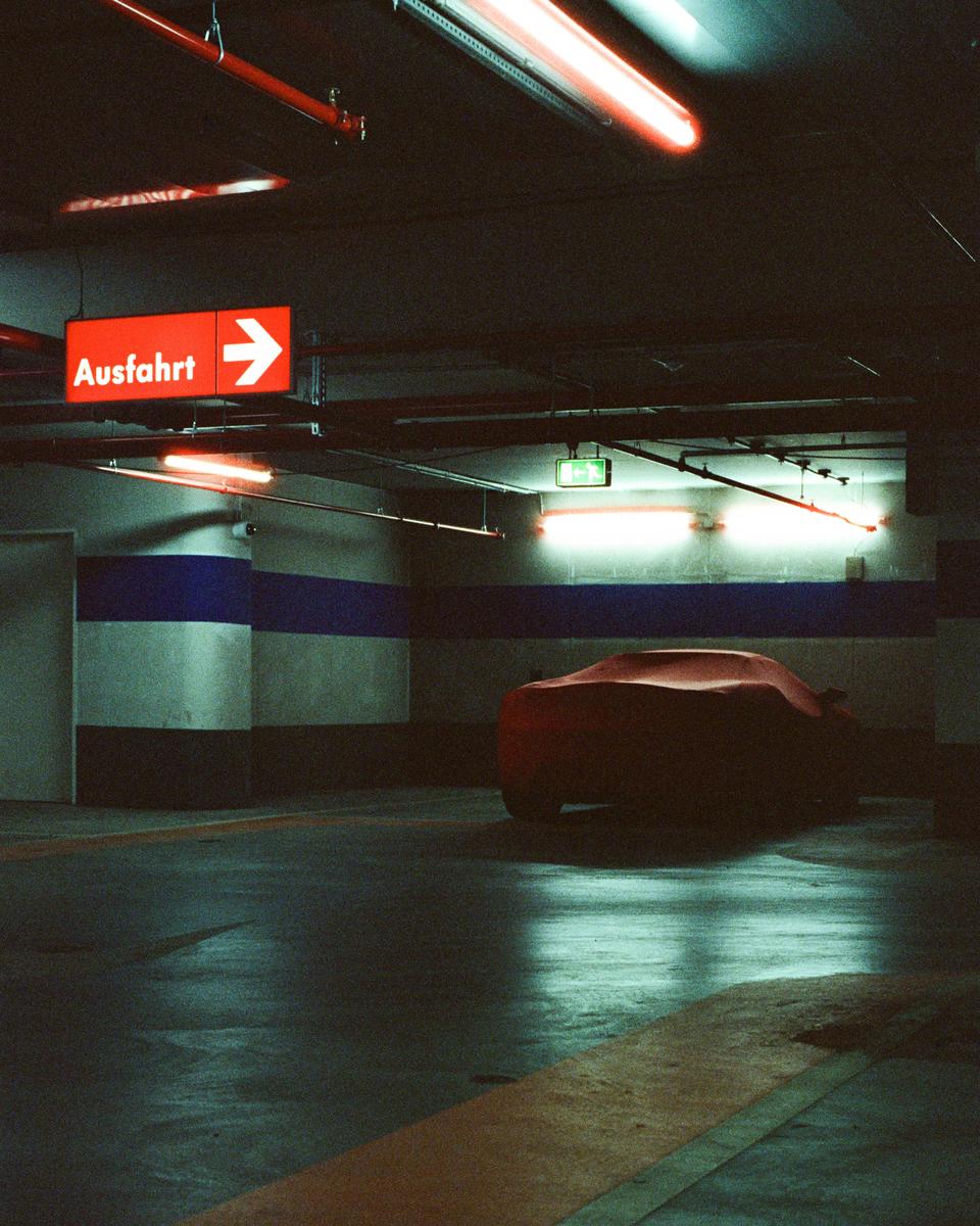 A red car cover is parked in a dark underground parking garage with an exit sign.