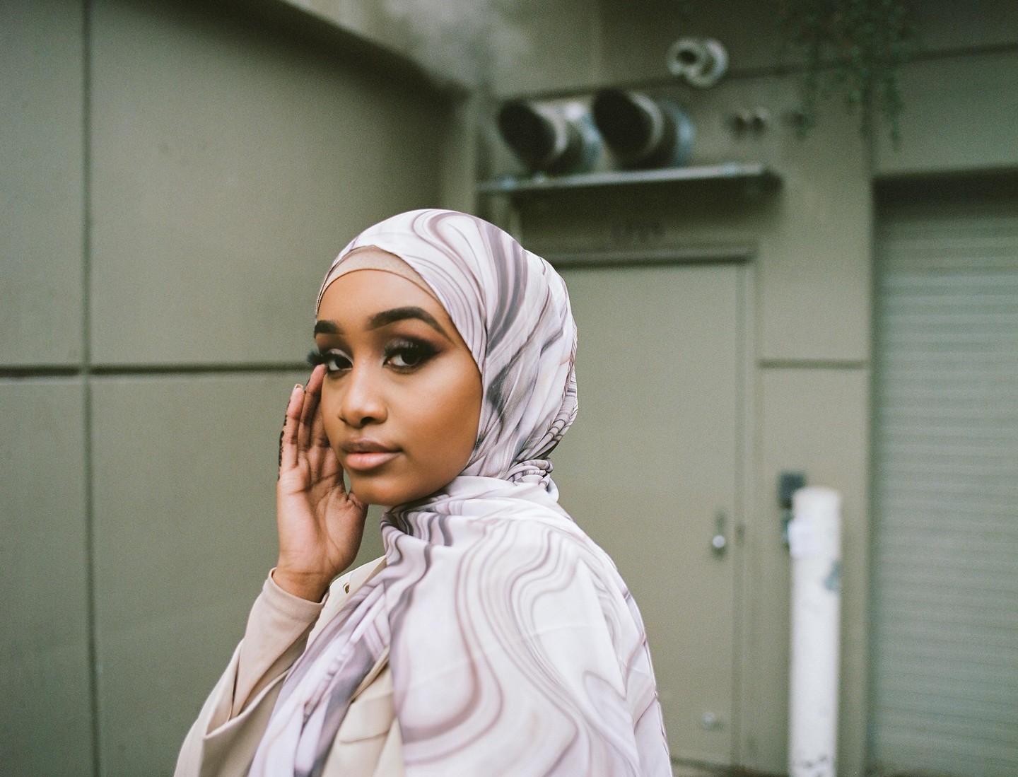 A woman wearing a patterned hijab poses for a portrait with her hand near her face.
