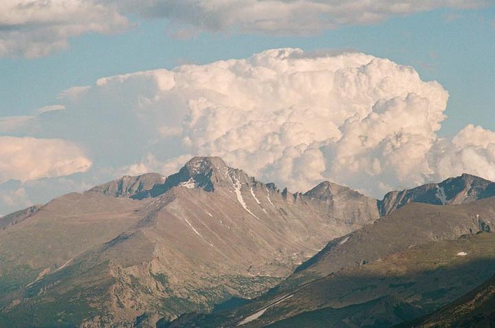 A large cloud formation looms over a mountain range with patches of snow.