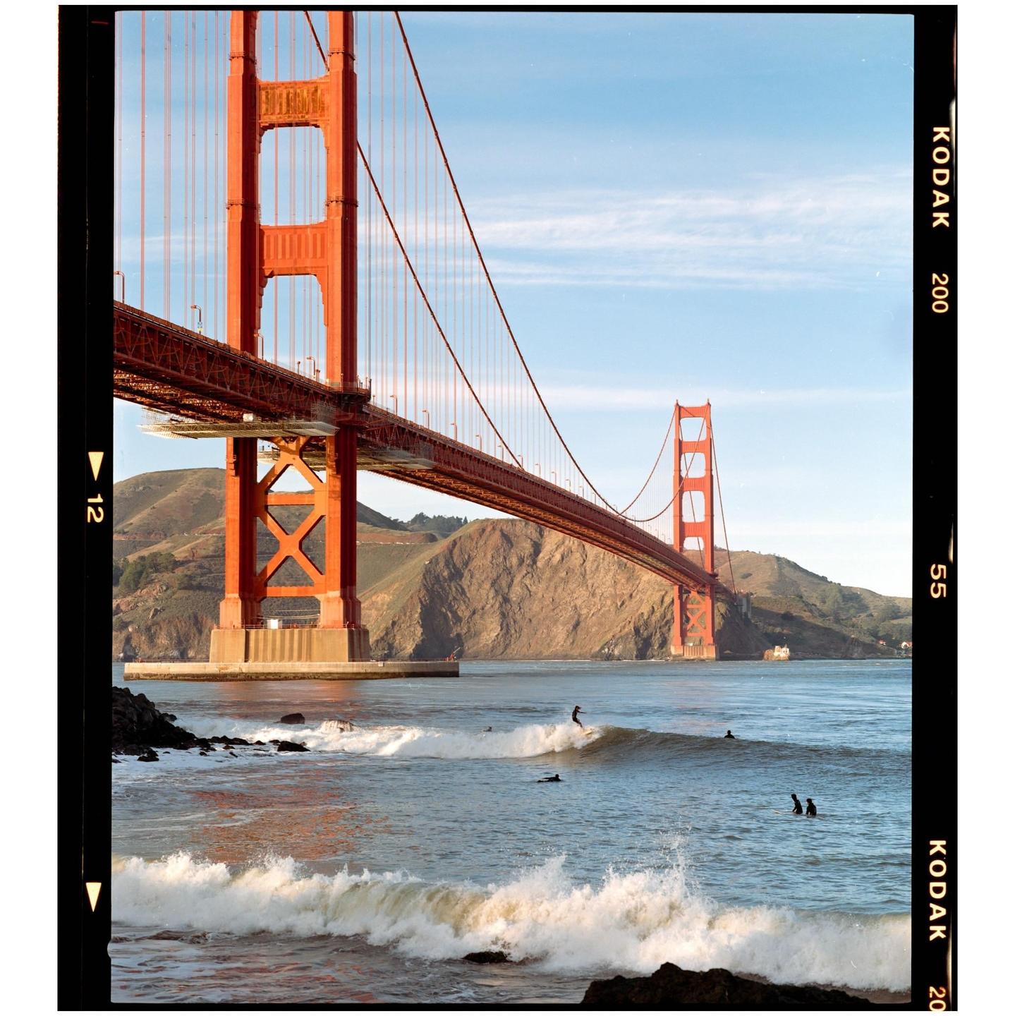 A surfer rides a wave in front of the Golden Gate Bridge.