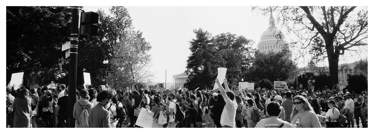 A large crowd of people protest in front of the Supreme Court building, with the Capitol building visible in the background.