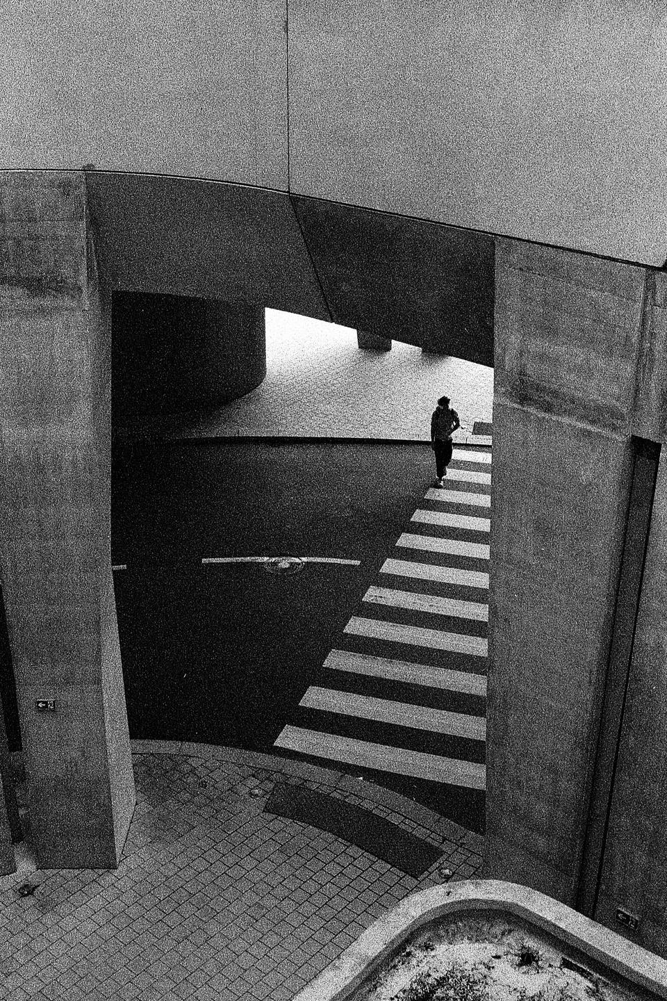 A person walks across a crosswalk under a concrete overpass.