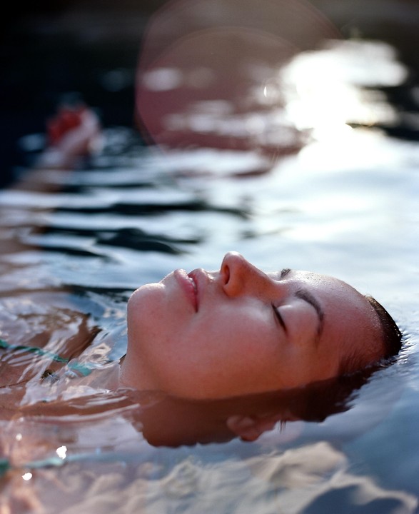A woman floats on her back in water with her eyes closed.