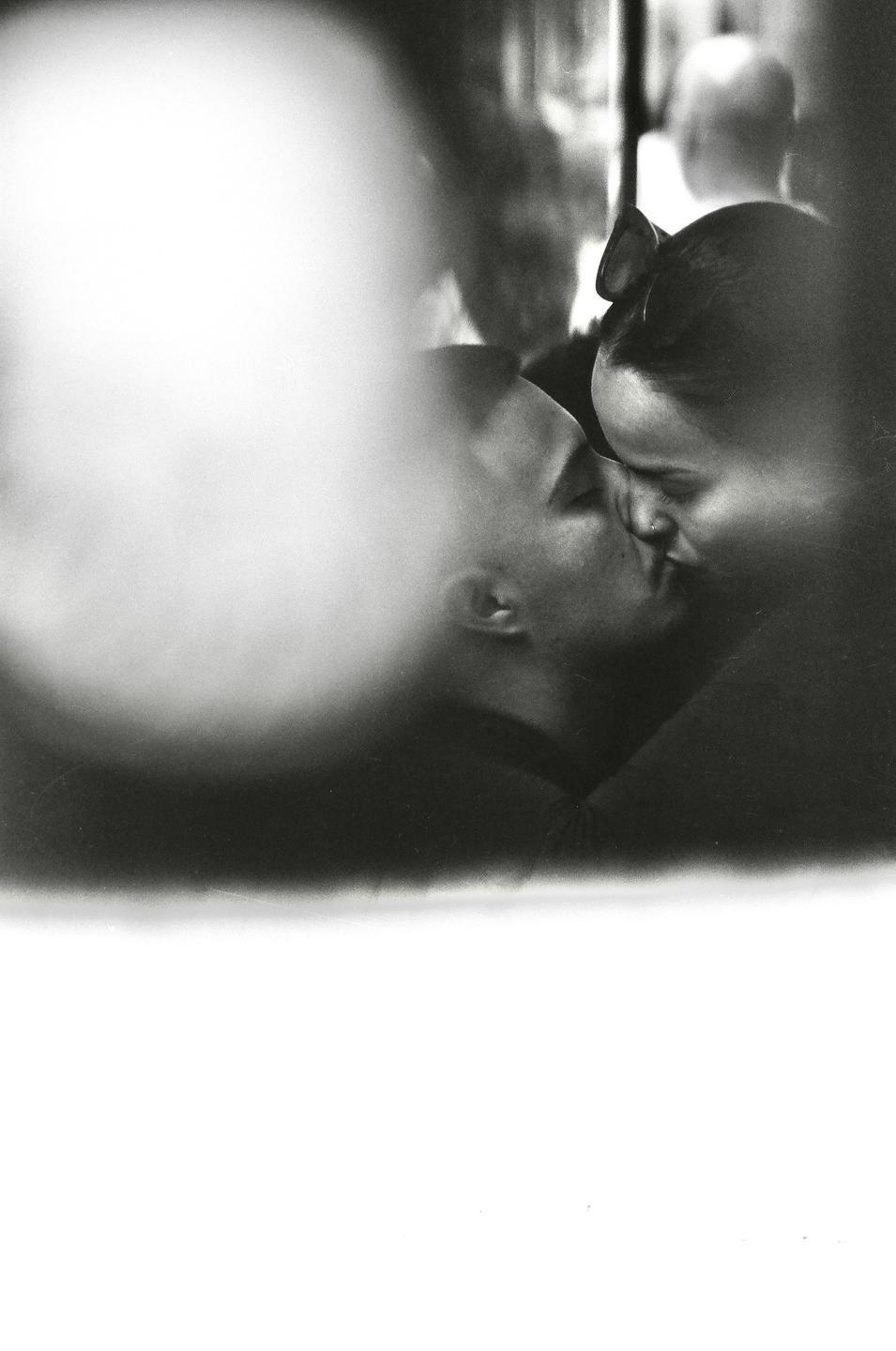 A couple kisses in a blurry, high-contrast black and white street photograph.