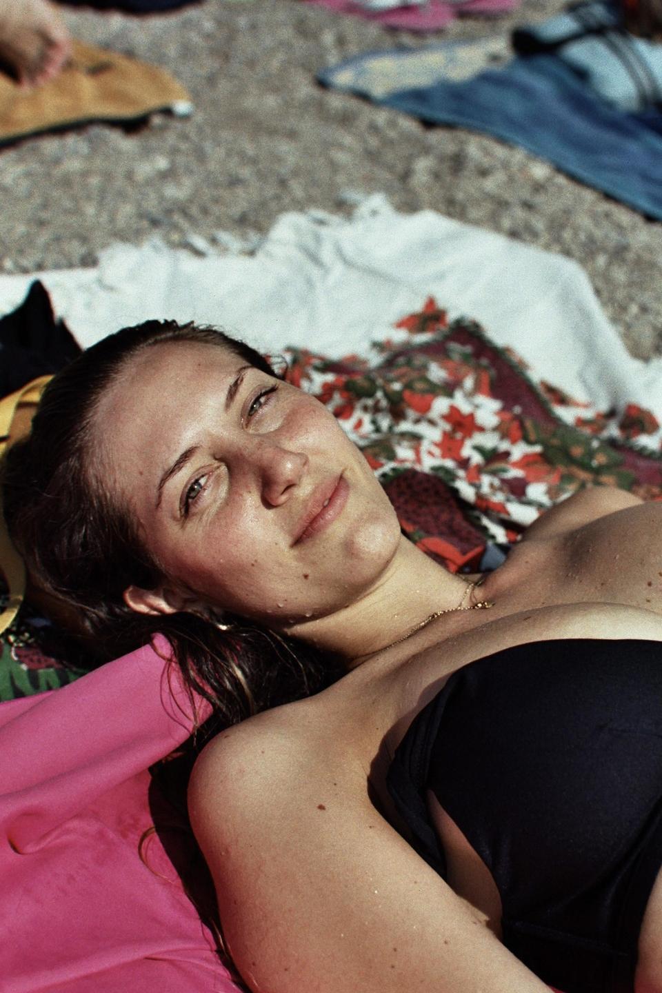 A woman with wet hair and skin lies on a blanket in the sun.