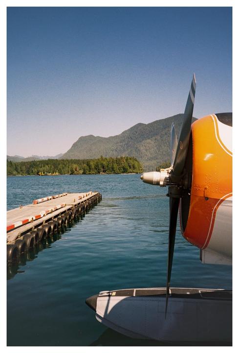 A seaplane is docked next to a pier on a lake with mountains and forest in the background.