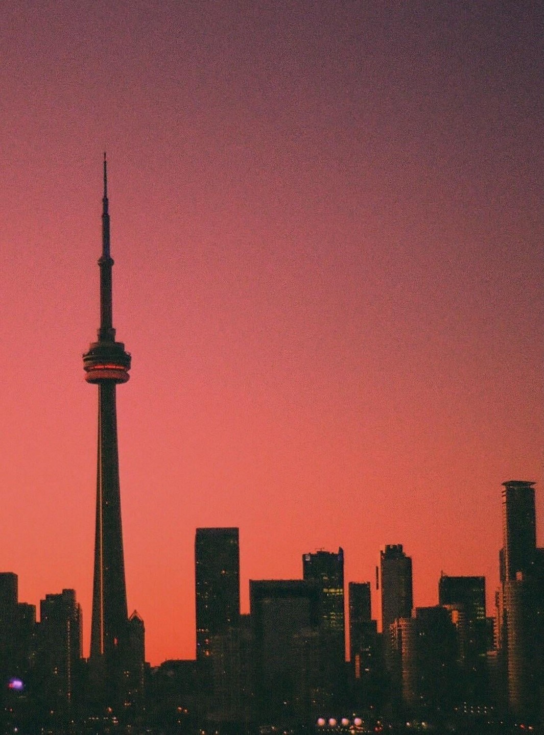 The Toronto skyline is silhouetted against a vibrant red and purple sky at dusk.