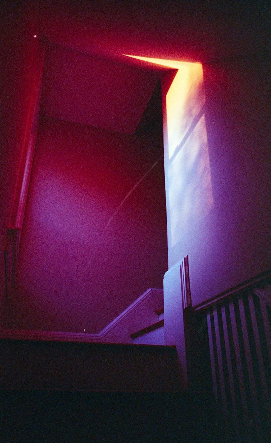 Light from a window illuminates a dark stairwell with a purple and red hue.