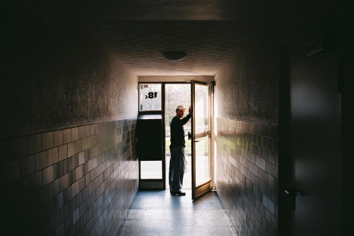 A man stands in a doorway at the end of a long, tiled hallway.