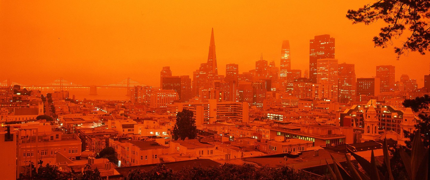 A panoramic view of the San Francisco skyline and Bay Bridge is bathed in an orange glow.