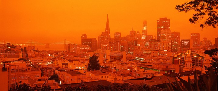 A panoramic view of the San Francisco skyline and Bay Bridge is bathed in an orange glow.