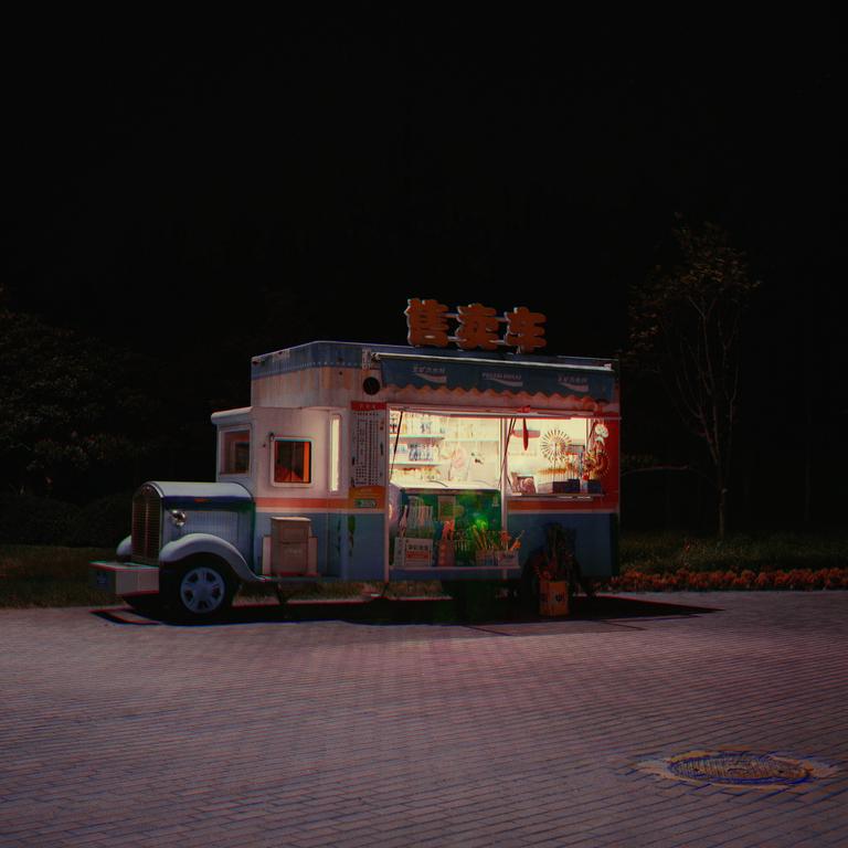 A food truck with glowing lights is parked on a paved surface at night.