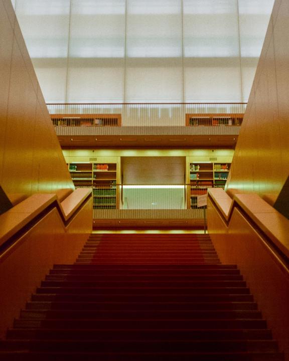 A red carpeted staircase leads up to a library with bookshelves and a balcony.