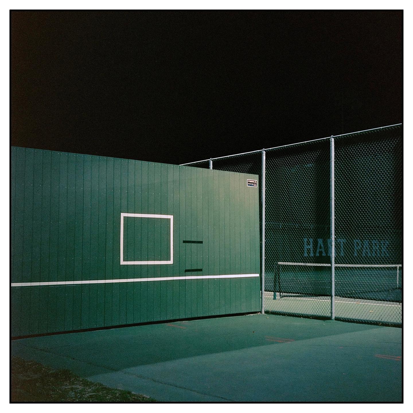 A green wall with a white square and line is next to a chain link fence at night.