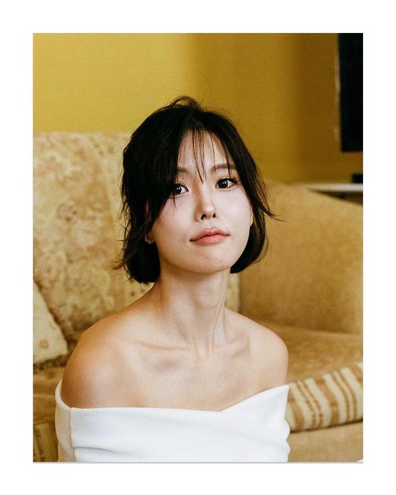 A woman with short dark hair and a white off-the-shoulder top poses for a portrait.
