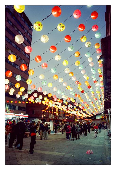 A street in Taipei is decorated with many colorful lanterns strung overhead, with people walking below.